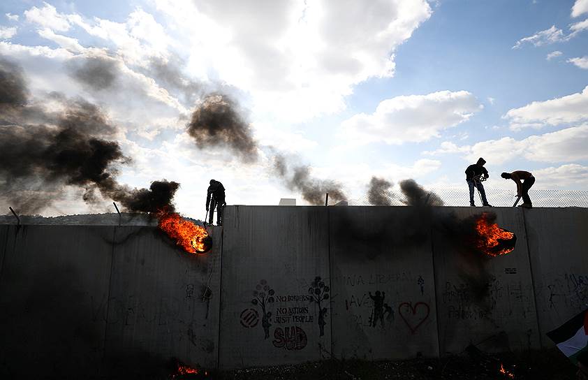 Билин, Палестина. Протестующие, стоя на заборе, поднимают горящие покрышки в знак протеста против сооружений на границе с Израилем