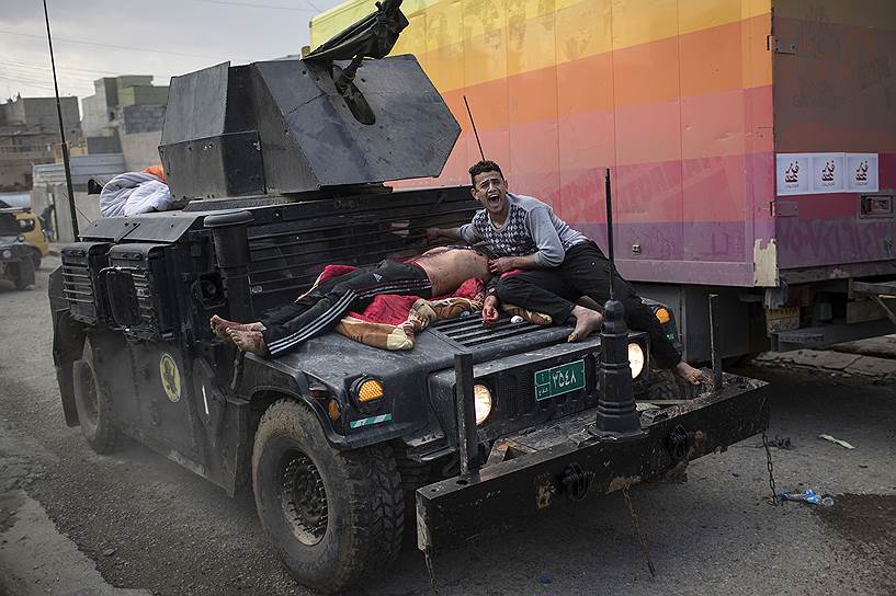 Мосул, Ирак. Местный житель помогает раненому мужчине, который лежит на капоте автомобиля правительственных войск