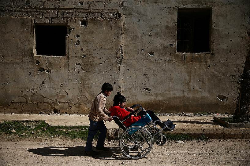Гута, Сирия. Мальчик везет своего друга с больным позвоночником в инвалидном кресле
