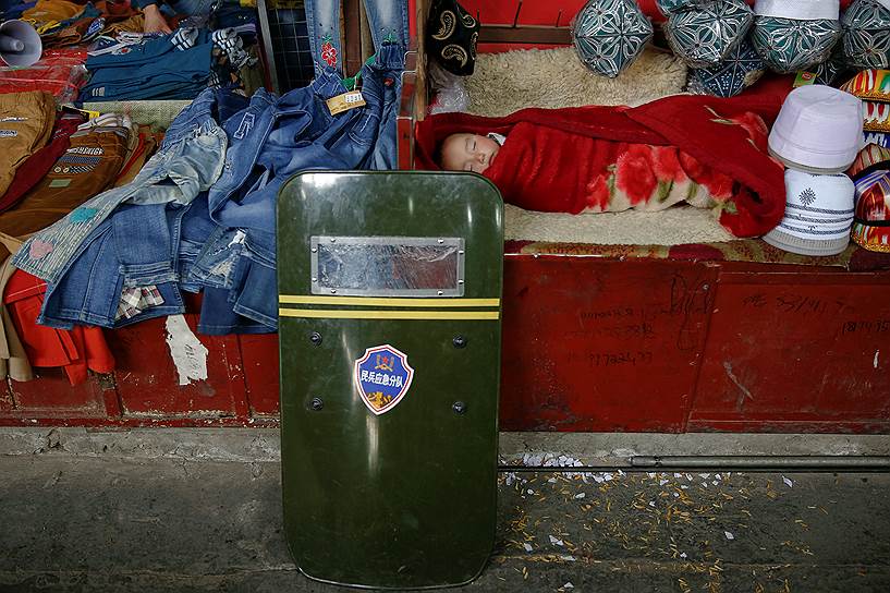 Девочка спит рядом со щитом полицейского в городе Хотан в СУАР