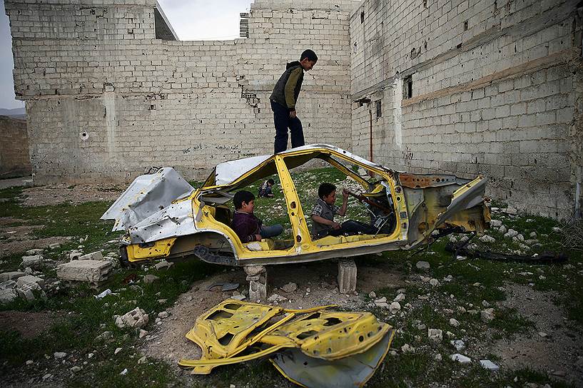 Дамаск, Сирия. Дети играют в каркасе автомобиля в разрушенном боями районе города