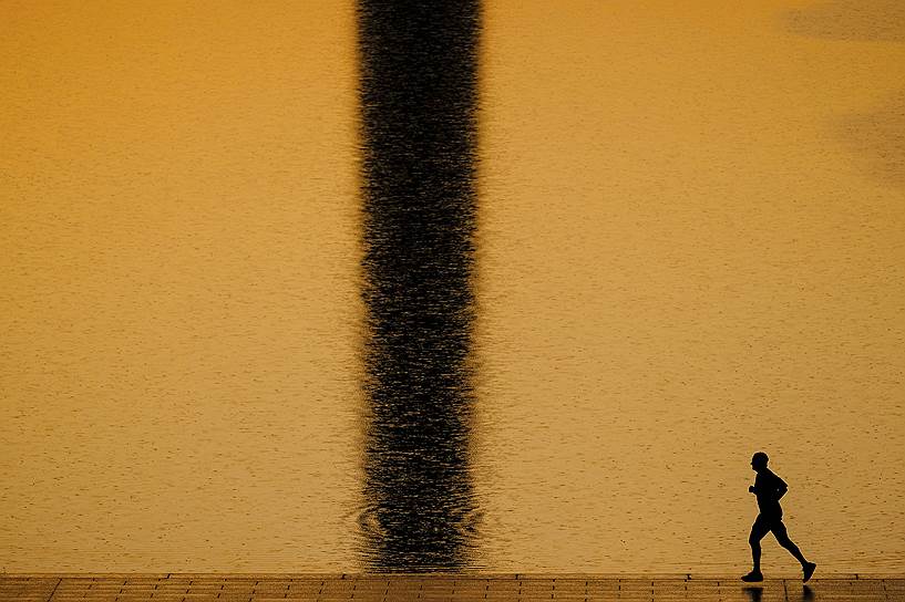 Вашингтон, США. Местный житель пробегает мимо Зеркального пруда, в котором отражается монумент Вашингтона