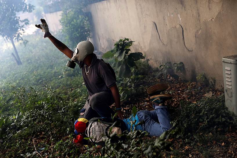 Каракас, Венесуэла. Участник антиправительственной акции помогает пострадавшему в столкновениях с полицией единомышленнику