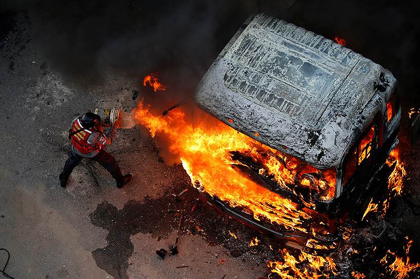 Каракас, Венесуэла. Пожарный пытается потушить горящую кабину грузовика, которую подожгли протестующие 