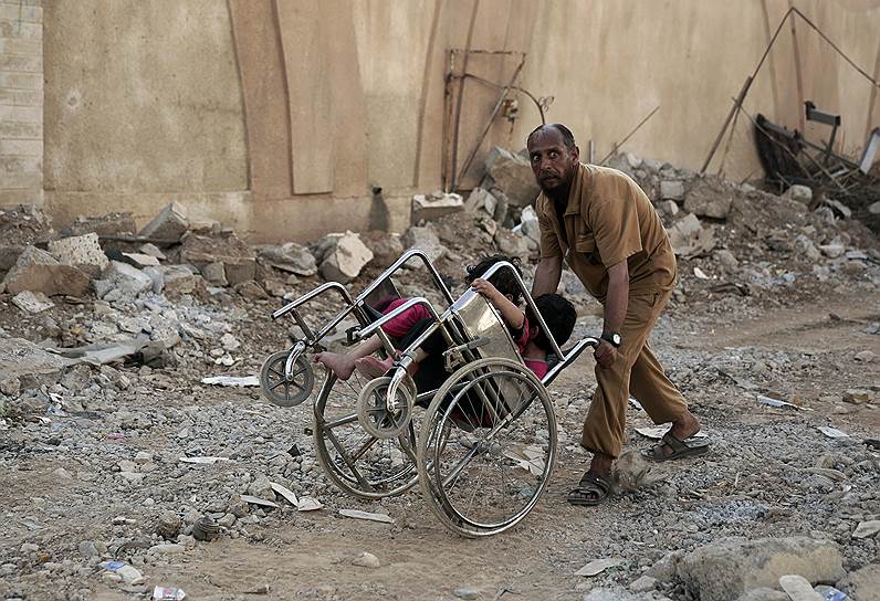 Мосул, Ирак. Мужчина везет детей в инвалидном кресле в разрушенной части города