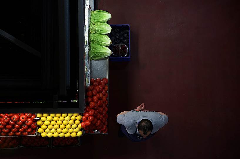 Мадрид, Испания. Продавец овощей ждет покупателей возле своего прилавка на рынке