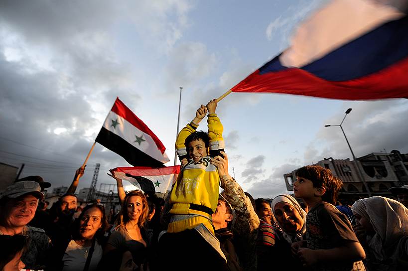 Хомс, Сирия. Местные жители размахивают сирийским и российским флагами после того, как последние повстанцы покинули город. В результате достигнутых договоренностей город полностью перешел под контроль правительственных сил 