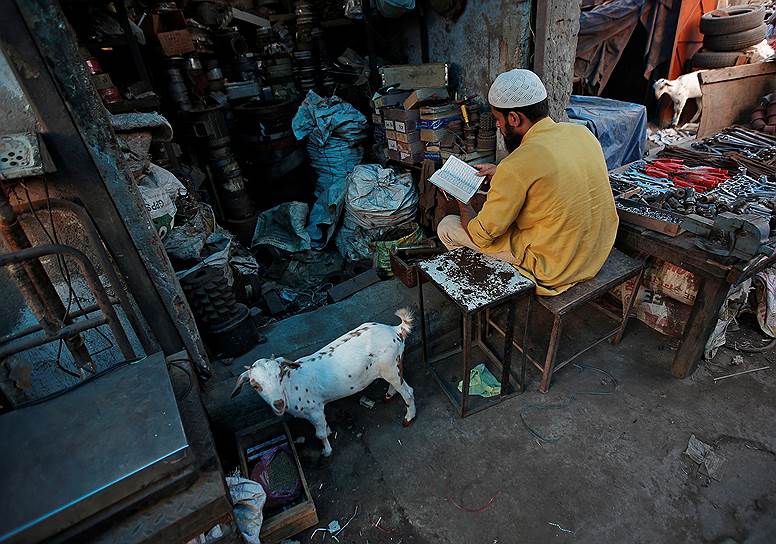 Дели, Индия. Мужчина читает Коран у входа в свою лавку 