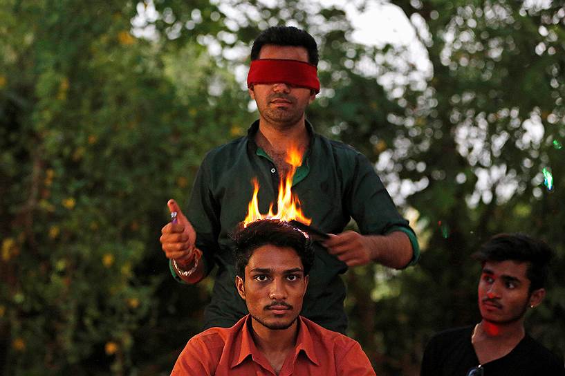 Ахмадабад, Индия. Парикмахер в повязке на глазах стрижет клиента огнем