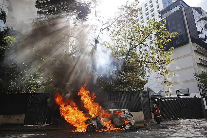 Каракас, Венесуэла. Пожарный пытается потушить автомобиль, подожженный во время акции против политики президента