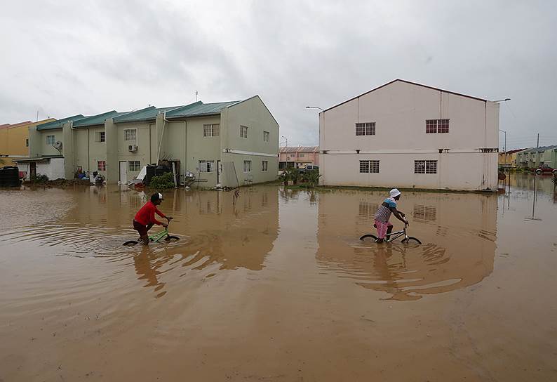 Оропун, Тринидад и Тобаго. Дети едут на велосипедах по затопленной улице