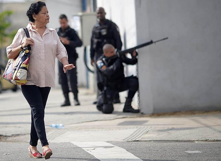 Рио-де-Жанейро, Бразилия. Местная жительница идет по улице, где полицейские проводят операцию по задержанию наркоторговцев