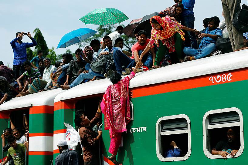Дакка, Бангладеш. Женщина помогает другой женщине забраться на крышу переполненного поезда