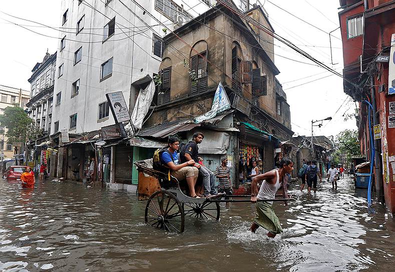 Калькутта, Индия. Извозчик помогает людям перебраться через затопленную от дождя улицу