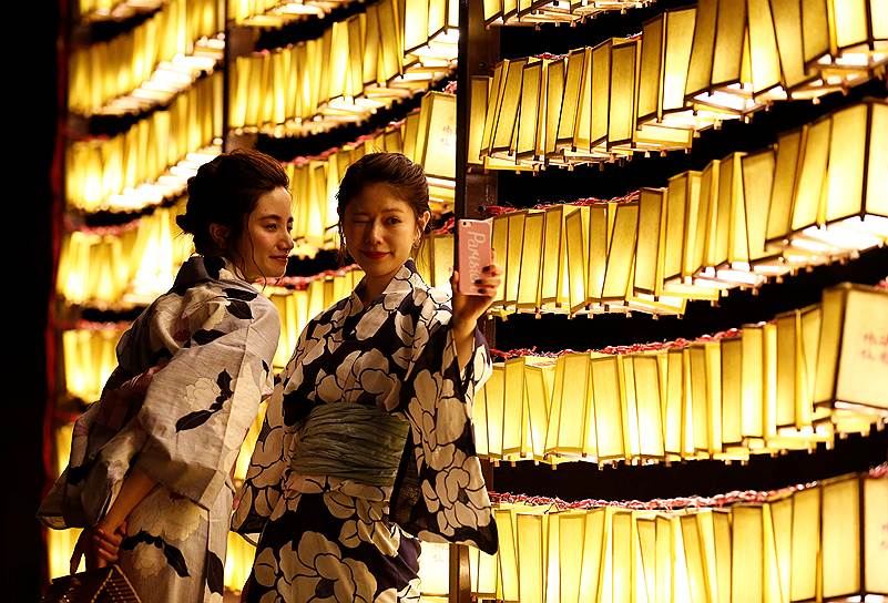 Токио, Япония. Девушки в повседневной одежде делают селфи напротив бумажных фонарей во время ежегодного фестиваля Митама