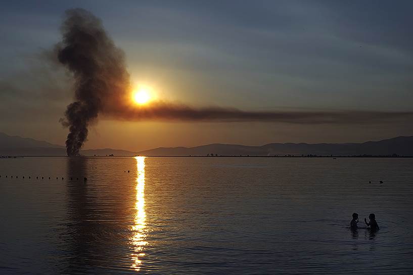 Керамоти, Герция. Дети плавают в море на фоне дыма от пожара и заката
