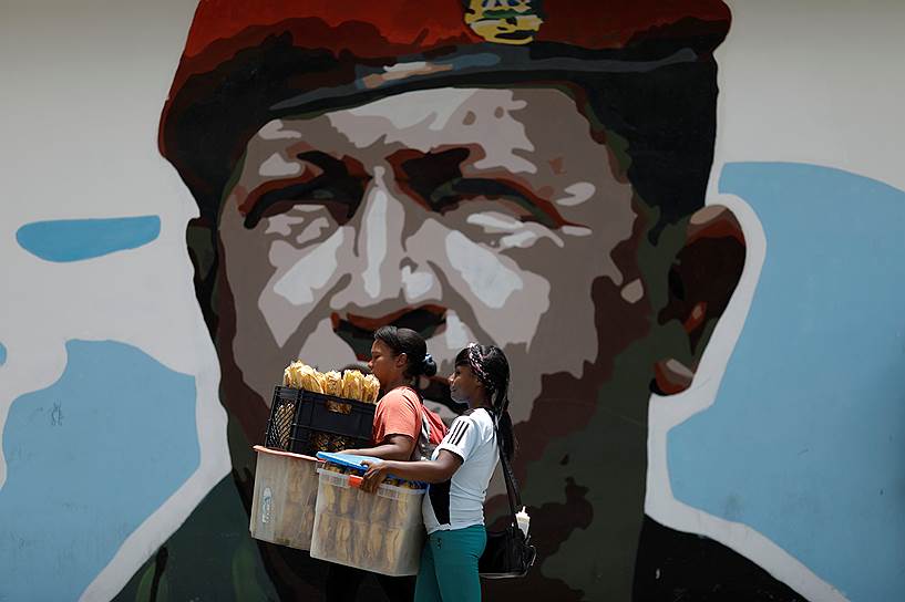 Каракас, Венесуэла. Проходящие мимо портрета покойного президента Венесуэлы Уго Чавеса женщины