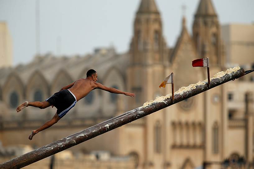 Сент-джулианс, Мальта. Мужчина пытается снять флаг с вымазанной жиром жерди во время праздника Святого Юлиана