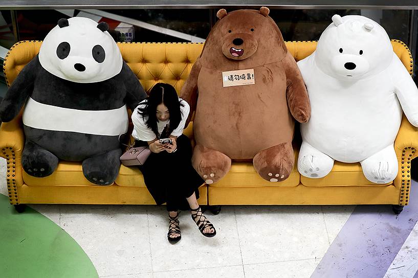 Пекин, Китай. Женщина смотрит в телефон, сидя на диване с плюшевыми игрушками в торговом центре