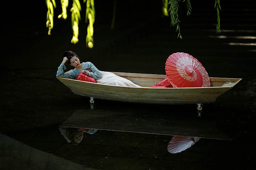 Пекин, Китай. Модель позирует, лежа в макете лодки, установленном в мелководном канале в парке