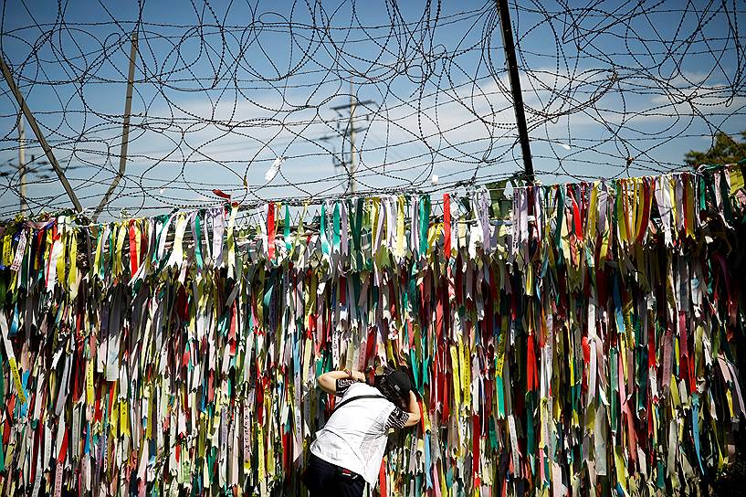 Пхаджу, Южная Корея. Женщина в районе демилитаризованной зоны заглядывает через забор, украшенный ленточками с призывами к объединению КНДР и Южной Кореи