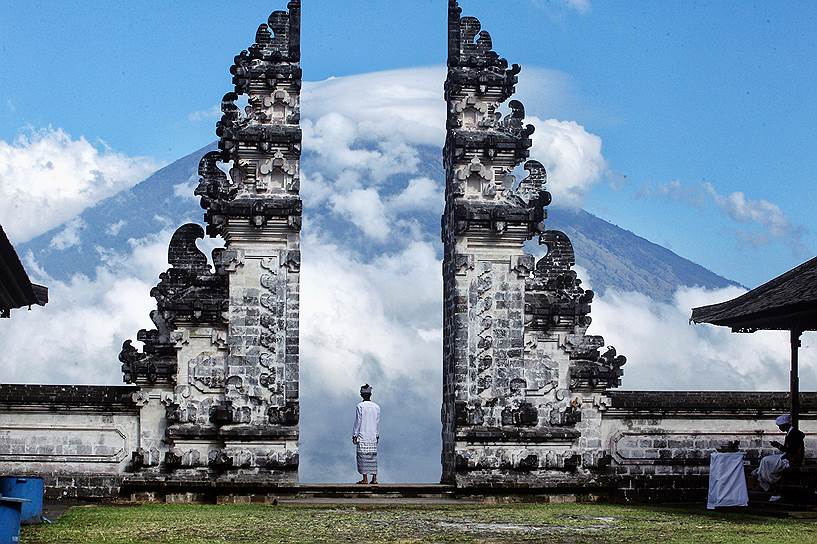 Карангасем, Бали, Индонезия. Местный житель стоит у храма и смотрит на вулкан Агунг