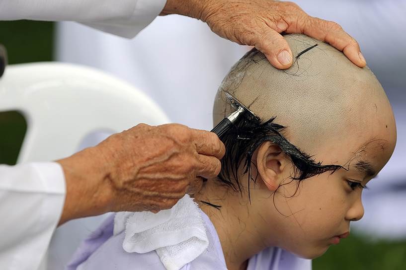 Бангкок, Таиланд. Монахиня стрижет девочку перед похоронной церемонией короля Таиланда Пхумипона Адульядета