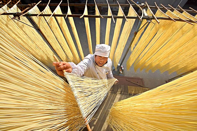 Линьи, Китай. Рабочий развешивает лапшу для просушки