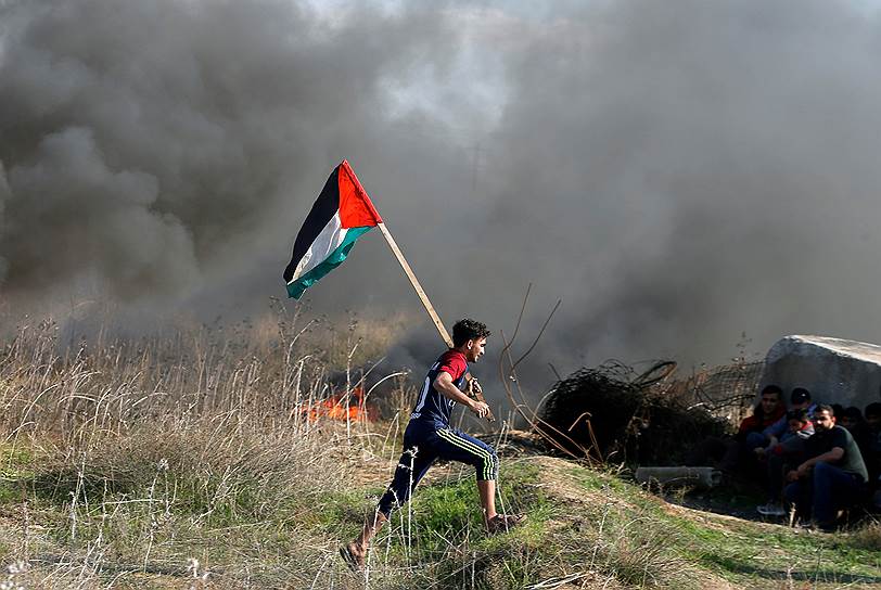 Сектор Газа. Протестующий с палестинским флагом убегает от израильской полиции