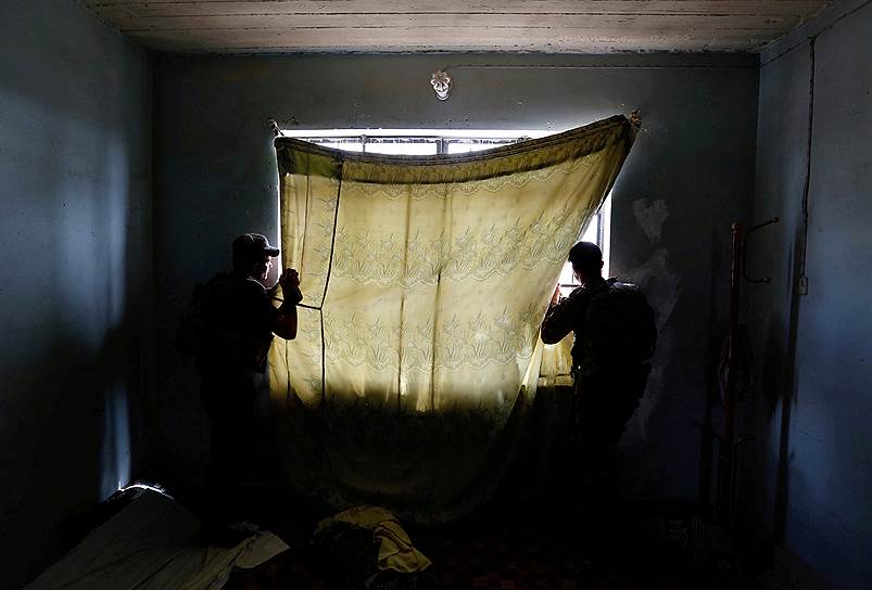 Члены контртеррористического подразделения выглядывают в окно, занавешенное покрывалом