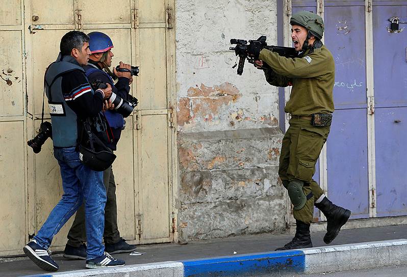 Хеврон, Западный берег реки Иордан. Израильский солдат направляет оружие на фотографов во время столкновений с палестинскими протестующими
