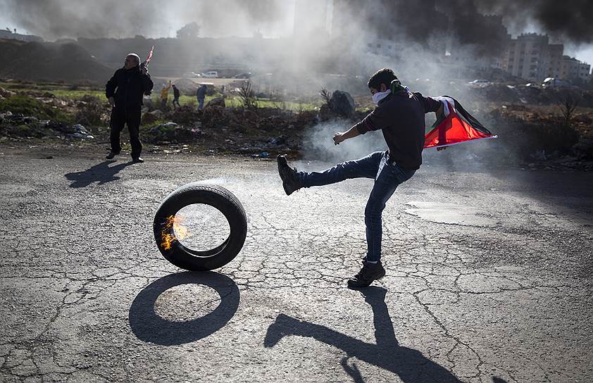 Рамалла, Западный берег реки Иордан. Палестинский протестующий пинает горящую шину во время беспорядков
