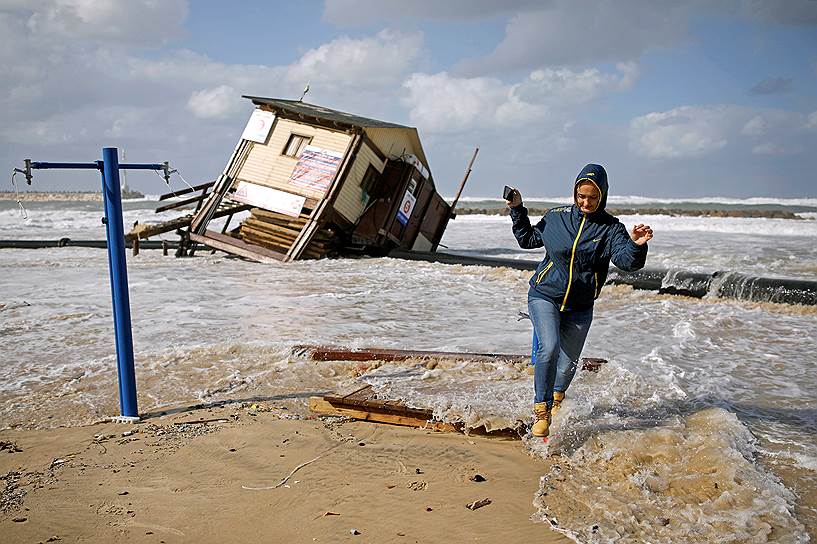 Ашкелон, Израиль. Женщина убегает от шторма на фоне разрушенной спасательной вышки
