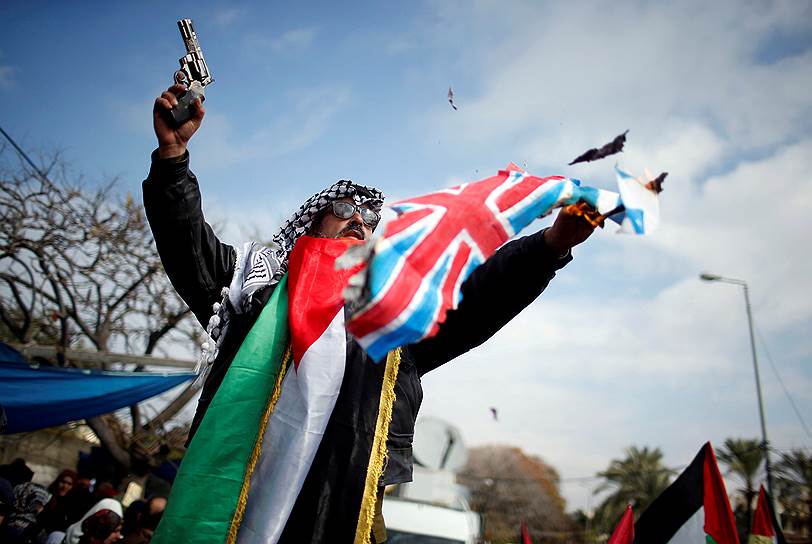 Газа, Сектор Газа. Палестинский протестующий сжигает израильский и британский флаги на демонстрации 