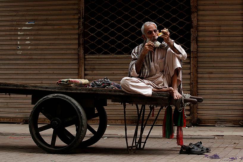 Карачи, Пакистан. Рабочий подстригает усы, сидя на своей тележке на рынке