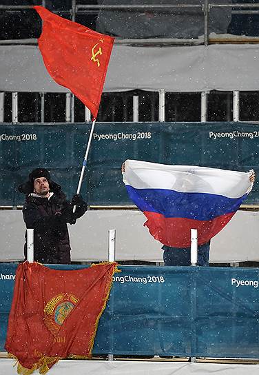 Российские болельщики держат российский и советский флаги во время лыжных гонок среди мужчин