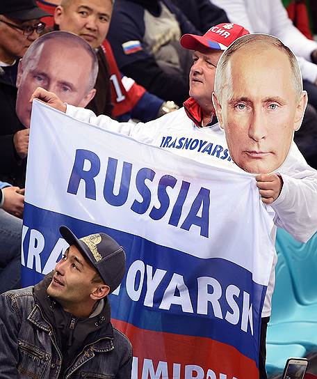 Болельщик из Красноярска держит в руках флаг России и маску президента Владимира Путина во время матча группового этапа по хоккею среди мужчин между Россией и США