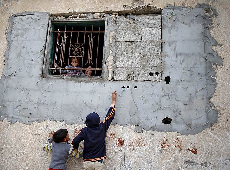Сектор Газа, Палестина. Мать с ребенком стоят у окна в то время как дети играют около их дома