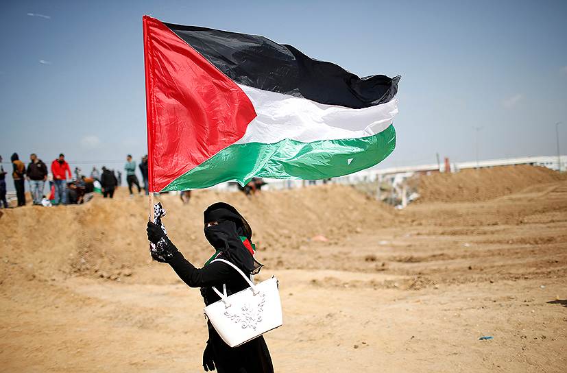 Сектор Газа. Местная жительница несет палестинский флаг в знак протеста 