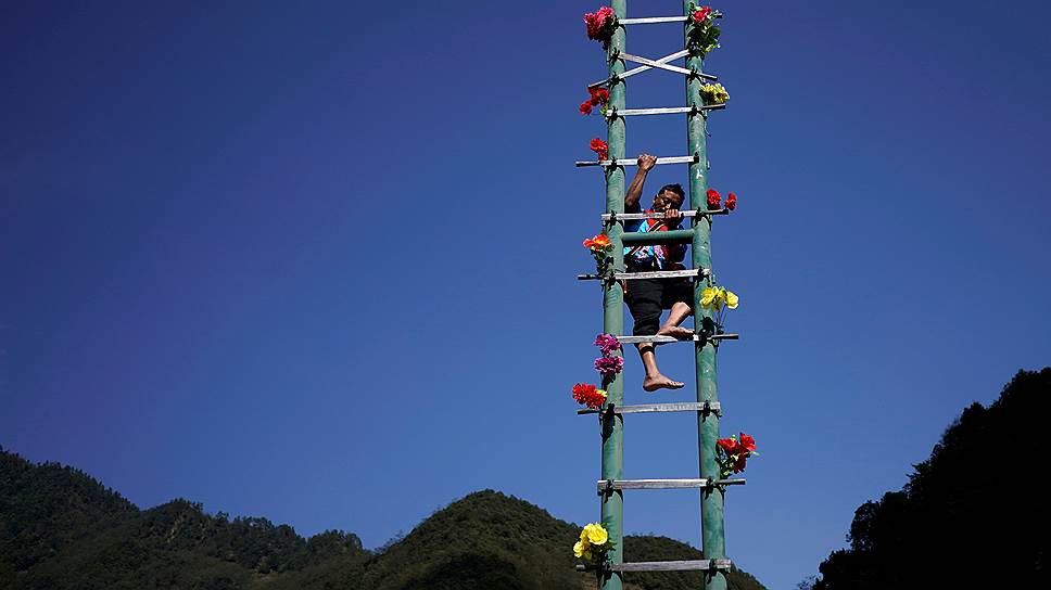 Провинция Юньнань, Китай. Представитель народа лису лезет по лестнице из ножей