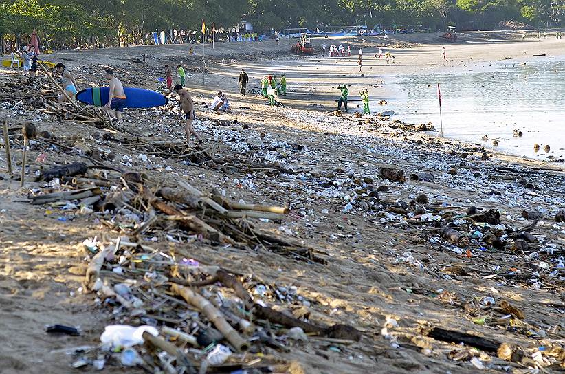 Бали, Индонезия. Туристы и коммунальные служащие среди прибрежного мусора