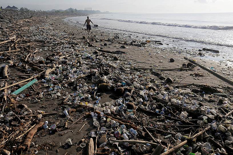 Санур, Бали, Индонезия. Местный житель бродит по загрязненному пляжу