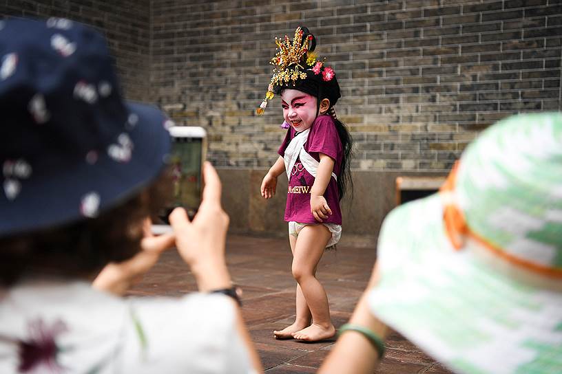 Панью, провинция Гуандун, КНР. Зрители фотографируют ребенка в национальном костюме