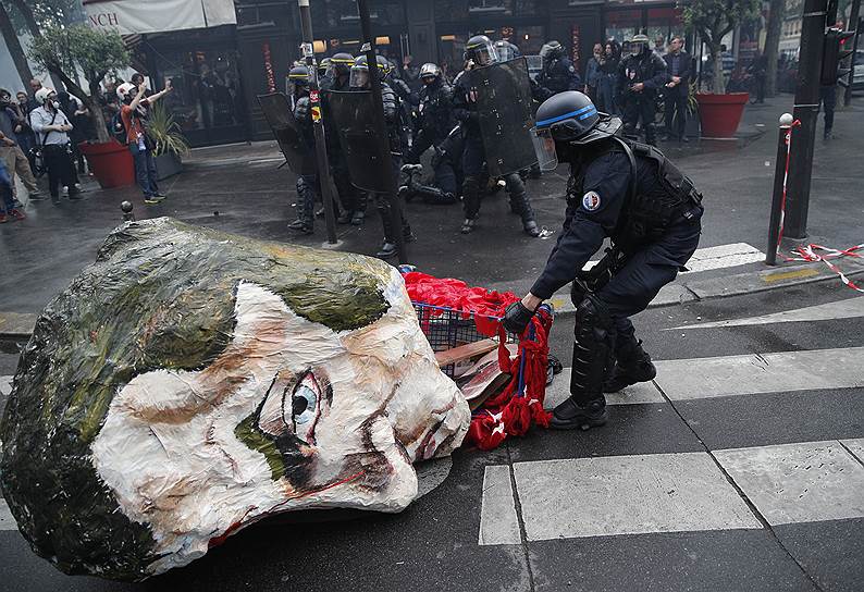 Париж, Франция. Полицейский убирает гигантскую маску президента Эмануэля Макрона на акции протеста профсоюзов