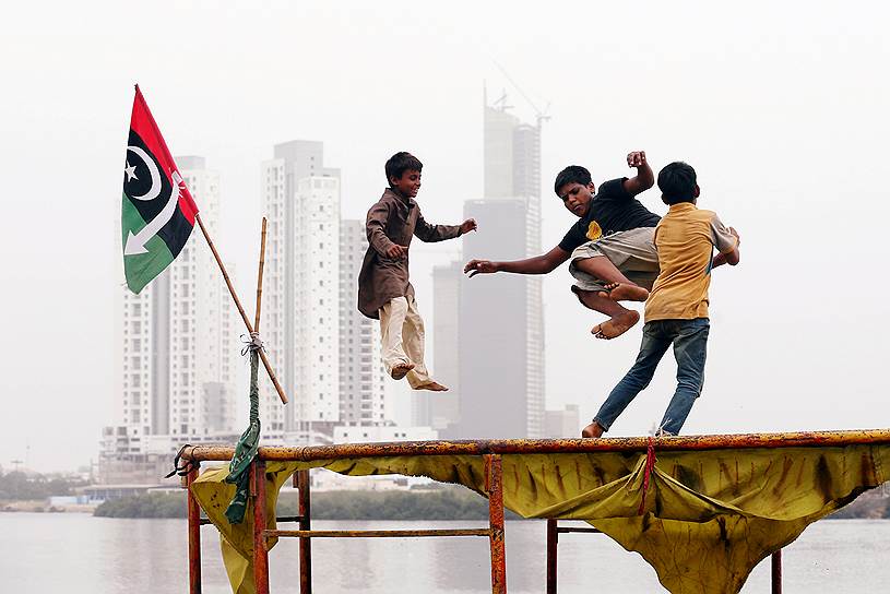 Карачи, Пакистан. Дети прыгают на батуте рядом с флагом одной из политических партий 