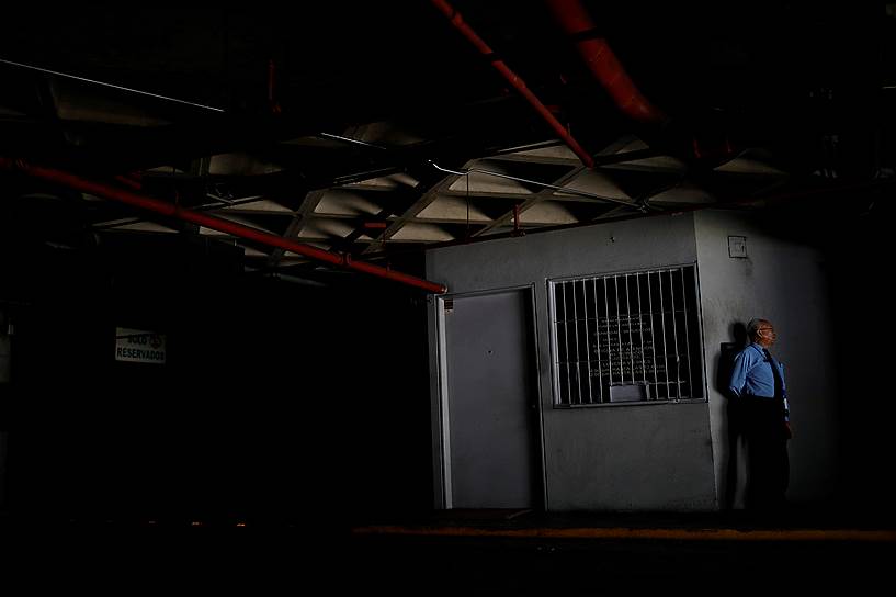 Каракас, Венесуэла. Охранник у входа на парковку во время отключения электричества