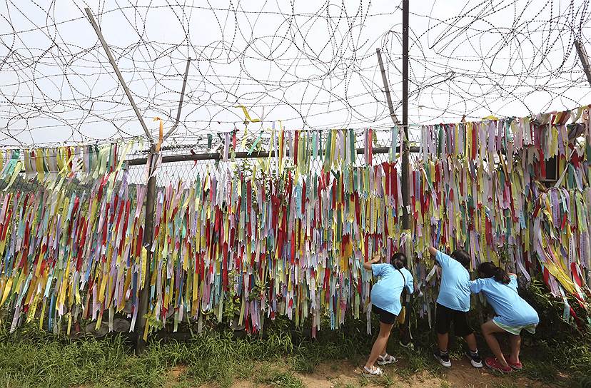 Южная Корея. Школьники смотрят через проволочный забор, украшенный лентами с сообщениями о желании воссоединения двух Корей