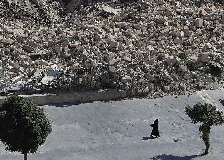 Алеппо, Сирия, Женщина проходит мимо разрушенных зданий