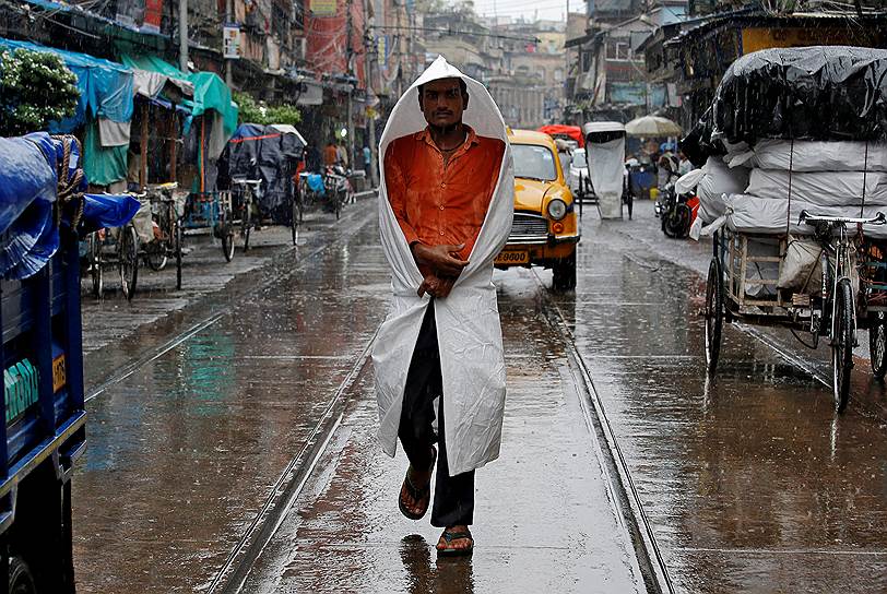 Калькутта, Индия. Мужчина, обернутый куском пластика, идет по улице под дождем