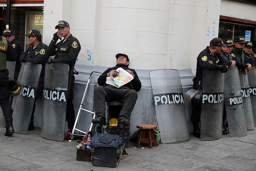 Лима, Перу. Чистильщик обуви отдыхает в окружении полиции, обеспечивающей порядок на акции протеста против коррупции 